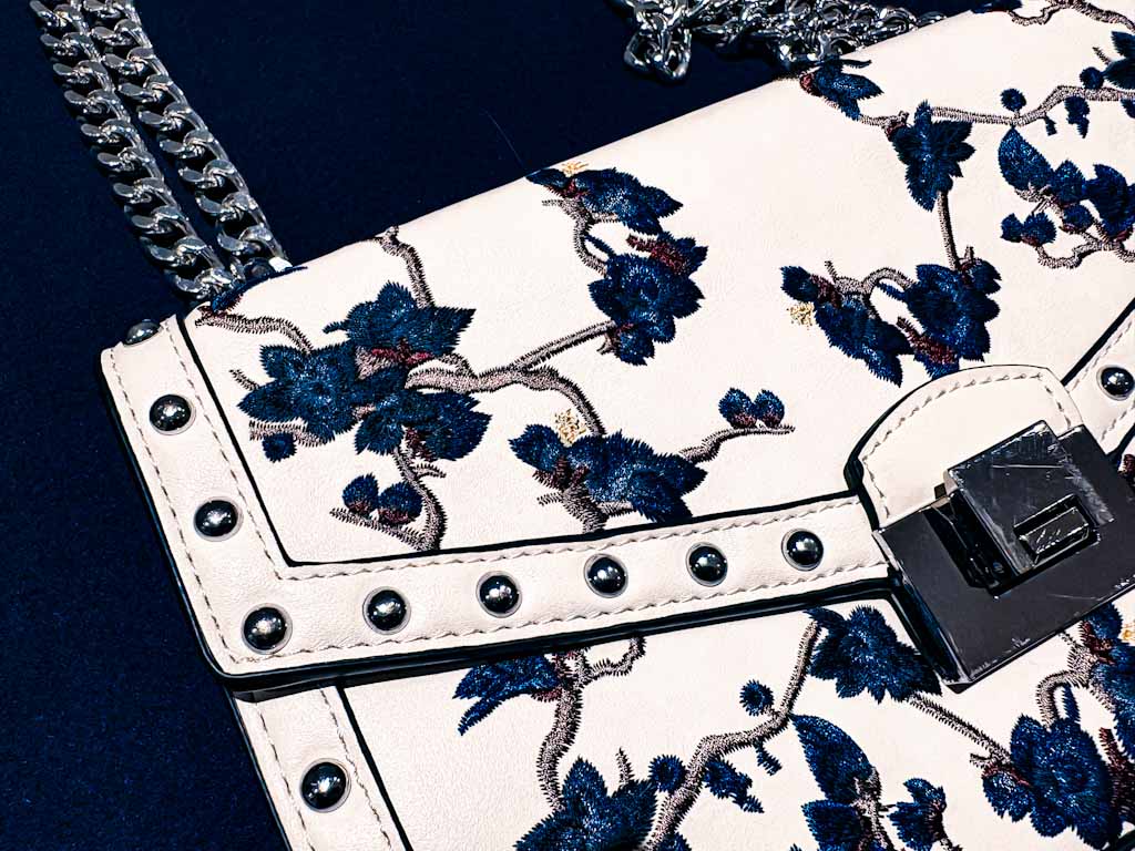 Bolso bandolera blanco con bordado floral azul y cadena plateada